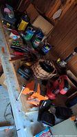 Photo showing a variety of tools, paint cans, hand tools, electrical tape, and a woven basket lamp base arranged on a white table.