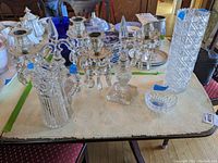 Full view of lot on table including candle holders with faceted crystal dangles, tall cut crystal vase, glass pitcher, and finger bowl among other tableware items