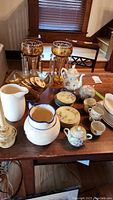 Photo of the full lot on table including candle lusters, porcelain tea set, pitchers, and small candle collars.