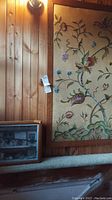 Large floral needlework embroidery hanging on wood-paneled wall