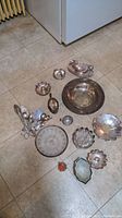 Full view of all silverplate and glass items arranged on floor, various bowls, utensils, candle holders shown.