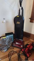 Full view of all items in lot showing vacuum cleaner upright, hand vacuum, fan, and vacuum bag box.