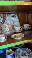 Shelf display of cups, saucers, divided plate with floral decoration, and mini pitchers.
