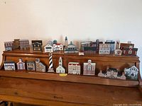 Front view of 22 wooden miniature houses and structures arranged on a wooden tiered display stand, showing various designs and colors.