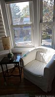 White upholstered armchair with slipcover style near window, needing cleaning.