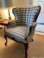 Side view of wingback armchair showing fabric upholstery and wooden curved leg.