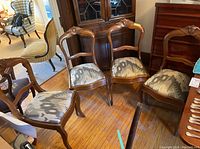 Four wood frame dining chairs with carved floral detail on backrests and gray patterned fabric upholstered seats grouped together on wood floor.
