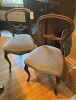 Two wooden framed chairs with light gray fabric upholstery placed side by side on a hardwood floor.