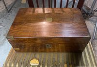 Closed view of the large wooden writer's desk storage box with a brass plate on top and a damaged keyhole escutcheon on the front.