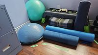 Wide view showing Bosu balance trainer, large green exercise ball, yoga mats, bench, and meditation cushion