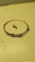 Wide view of the gold bangle and small pin on a flat surface showing overall design and condition