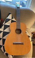 Full view of Harmony F-63 classical guitar showing body and part of neck on a couch.