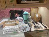 Wide view of multiple kitchen items on counter including glass weights, serving tray, cutting boards, skewers, mortar and pestle, grater and various utensils