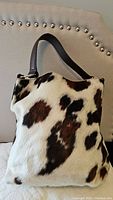 Front view of cowhide pattern purse with brown and black spots on white fur and dark brown leather handle.