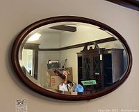 Full view of the oval wall mirror hung on a wall, showing wood frame and reflection in glass.