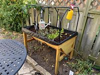 Front/side view of outdoor planter with plants, black mesh liner, plastic tubing arches above, and metal floral watering can inside.