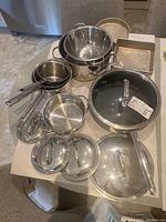 Photo showing the collection from above including the colander, frying pans, saucepans, baking pans, and lids arranged on a table.