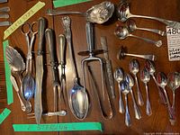 Full view of the various silver plated cutlery laid on a wooden surface including forks, spoons, knives, and tongs, showing array of utensil types and styles.
