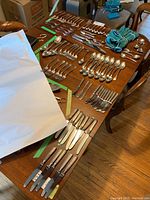 Wide view of the entire lot laid out on the table showing various forks, knives, spoons, and serving pieces along with wrapping paper.