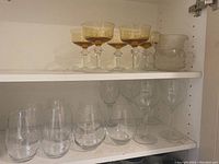 Amber-tinted stemmed glasses with clear stemmed wine glasses on two shelves
