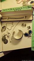 Overview of sterling silver jewelry lot with bracelets, earrings, and bangle including green sticker noting 14k gold plated marking.