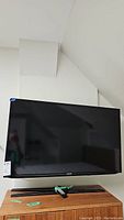 Samsung 46-inch TV mounted on wall with converter below on wooden cabinet, showing front view.