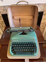 Optima manual typewriter inside its open carrying case placed on a wooden table, showing the keyboard and part of the paper holder mechanism.