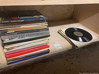 Stack of vinyl records including The Mikado, H.M.S. Pinafore, Concert Favourites and a loose record on the shelf showing scratches.