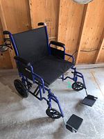 Side view of a blue Drive bariatric transport wheelchair showing black padded seat and armrests, large rear wheels and footrests.