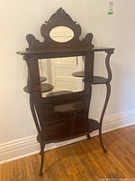 Front view of wooden display shelf showing oval and rectangular mirrors, curved legs, and multiple shelves for display.