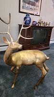 Full view of the large brass deer sculpture showing body and antlers in room setting.