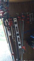 Clamps and metal level hanging on wooden wall inside garage with daylight