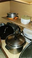 Photo showing metal pots, cast iron pans, and stacked Corning Ware casseroles with plastic lids inside cabinet.