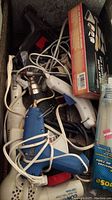Overview of assorted heating tools including glue guns, hair dryers, glue sticks and power cords piled together showing condition and variety.