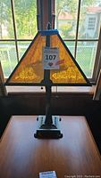 Front view of the lit lamp showing amber colored plastic panels with metal frame and base