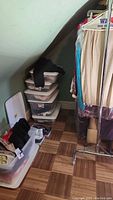 Photo of storage tubs with clothing stacked in attic corner near angled wall.