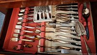 View of full flatware set with multiple types of utensils organized in a wooden drawer with red lining.