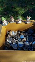 Overall view of box containing various metal beer stein lids and four figural ceramic stein tops depicting German men and a musician.