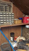 Shelf with multiple plastic hardware storage boxes containing small drawers, a glass jar, and a tool belt or apron on lower shelf.
