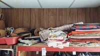 Photo of a shelf with multiple folded upholstery fabrics, including striped and floral patterns, along with other stored items in a garage setting.