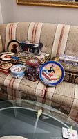 All tins displayed on a striped sofa showing various shapes, sizes, and decorative styles including Disney Mickey Mouse and Christmas themes
