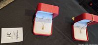 Two necklaces displayed in red jewelry boxes, one with a diamond pendant and the other with a pearl pendant.