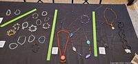 Overview of jewelry lot with multiple necklaces displayed on black cloth, three necklaces feature jade pendants or medallions separated by green tape.