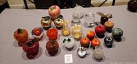 Full collection of decorative apple figurines arranged on table showing variety of materials including glass, metal, crystal, and stone