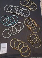 Top-down close-up photo showing varied colored bangle bracelets arranged in groups on a black surface including silver, gold, turquoise, and multicolor stone bangles.