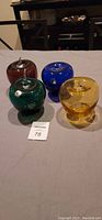 Four Blenko handmade glass apples in amber, green, blue, and brown colors arranged on a table