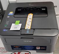 Front and top view of a Brother HL-L2320D printer showing paper feed, control LEDs, brand logos, and feature stickers.