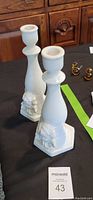 Pair of white ceramic candle holders shown on table with close-up of cherub detail
