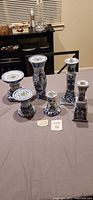 Set of six blue and white ceramic candle holders from the Canton Collection arranged on a table, showing varying sizes and shapes with floral motifs.