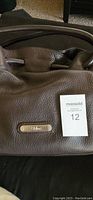 Close-up of brown leather Cole Haan handbag showing texture and metal plaque